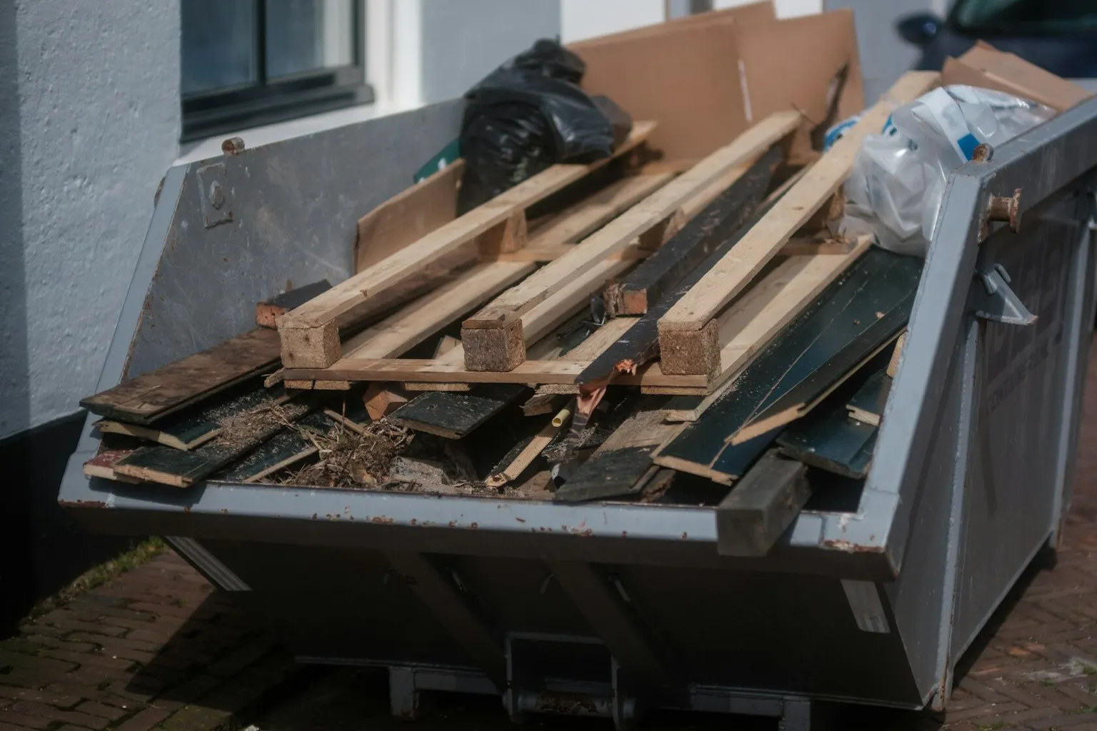 Absetzcontainer mit Holz und Verpackungsresten vor einem Gebäude
